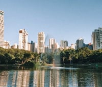 Skyline de Goiânia ao entardecer, prédios e áreas verdes ao redor de um lago.