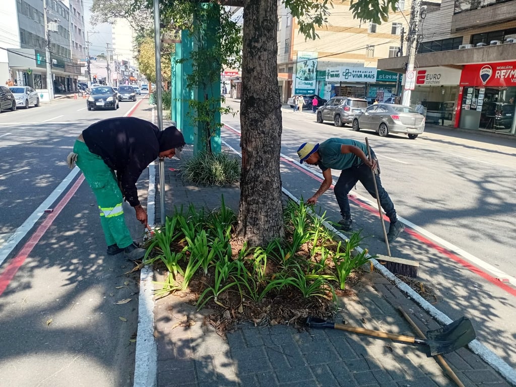 Profissionais de serviços urbanos realizando jardinagem e limpeza com EPIs em área pública