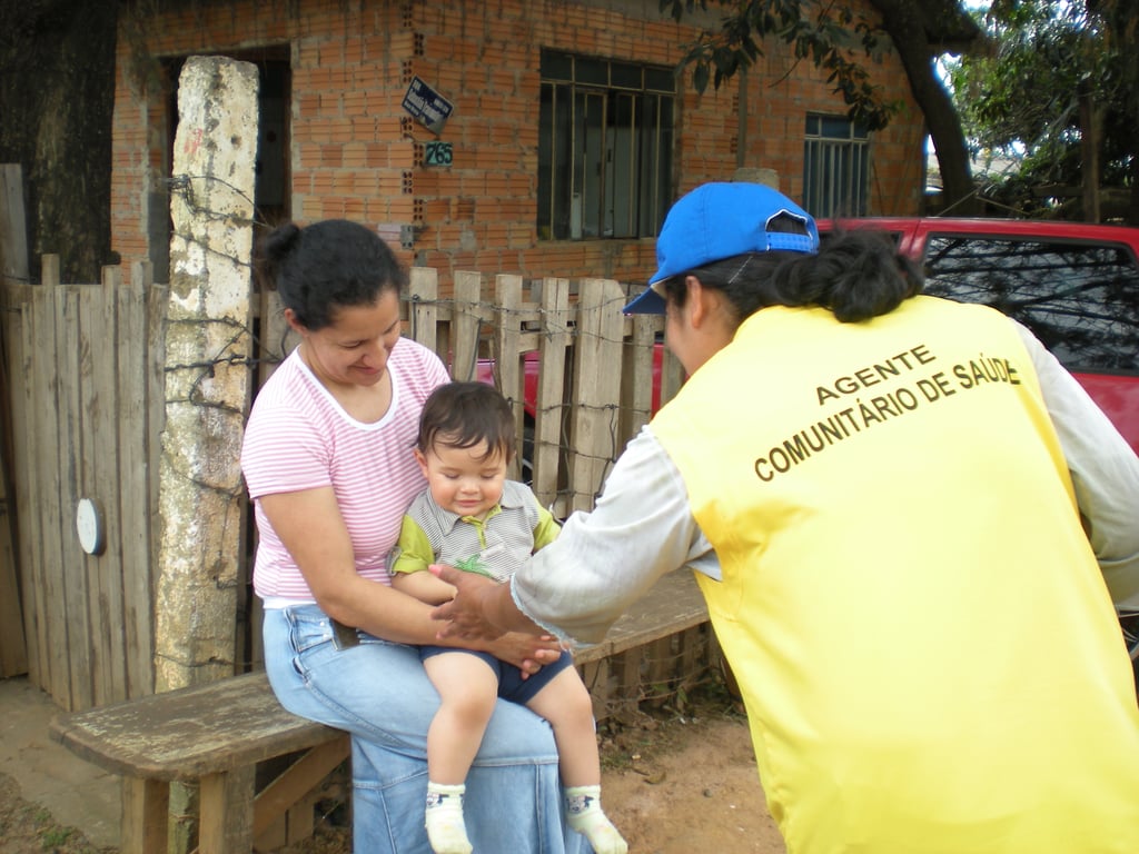 Agente comunitário de saúde em visita domiciliar em cenário urbano simples.