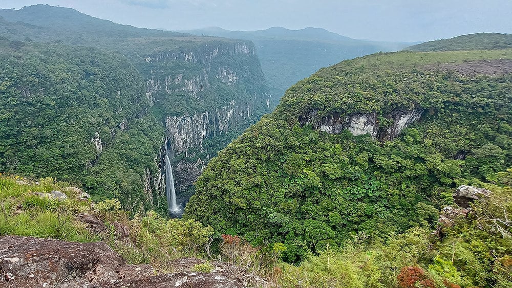 Paisagem do interior do Rio Grande do Sul ao entardecer, com relevo suave e queda d’água ao fundo