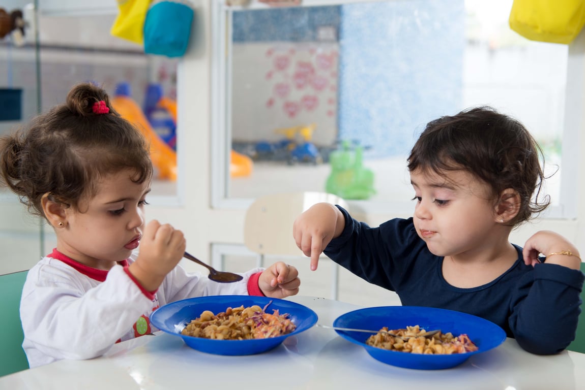 Crianças em refeitório escolar com refeições saudáveis servidas em bandejas