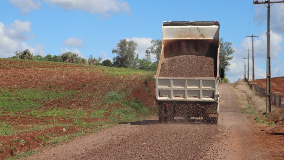 Estrada vicinal de terra batida em área rural, com caminhão descarregando materiais