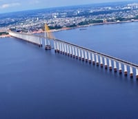 Vista aérea da Ponte Rio Negro ao entardecer, conectando Manaus a Iranduba AM, com o rio e a floresta ao fundo.