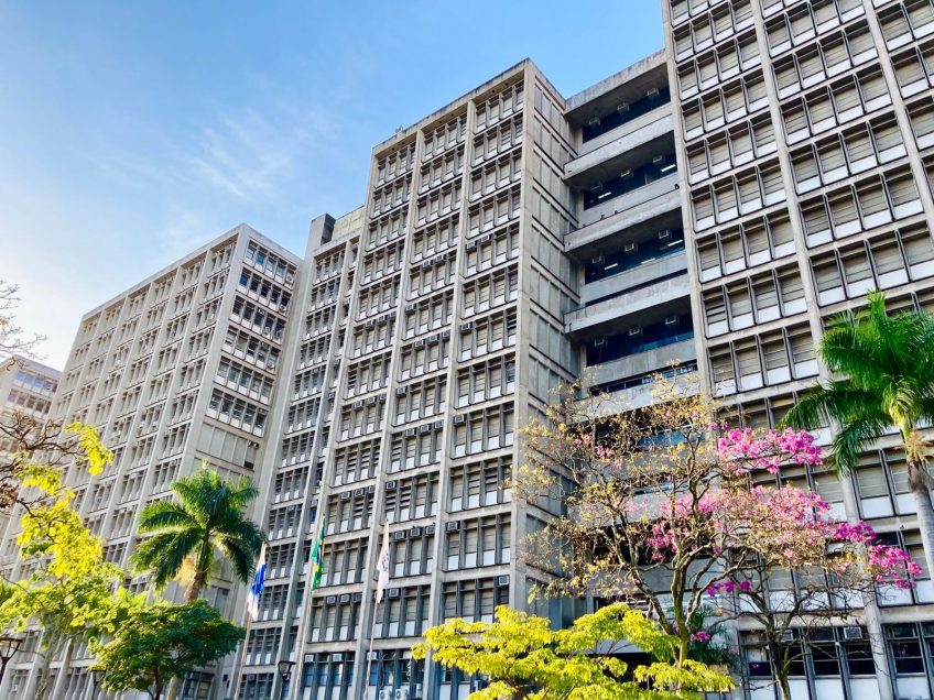 Fachada de prédio universitário público, com paisagismo e céu claro