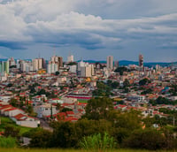 Vista panorâmica do centro de Varginha MG, com edificações e casas sob céu parcialmente nublado