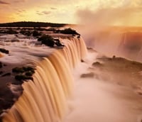 Foto panorâmica das Cataratas do Iguaçu ao entardecer, mostrando a força das quedas e a natureza ao redor