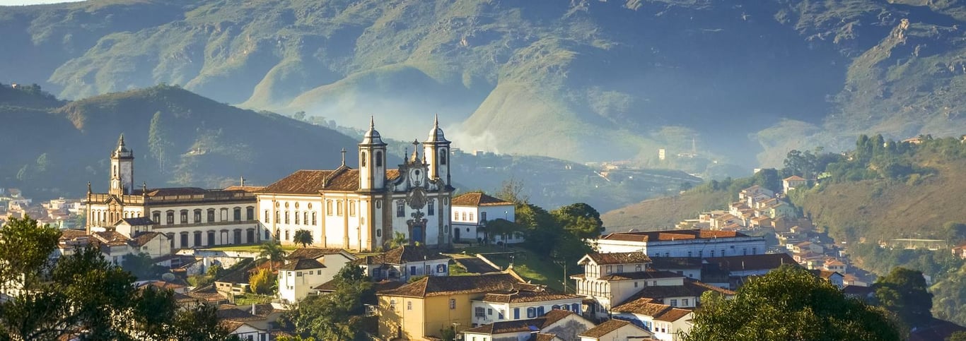 Vista panorâmica de Ouro Preto, com casario colonial e igrejas barrocas ao entardecer.
