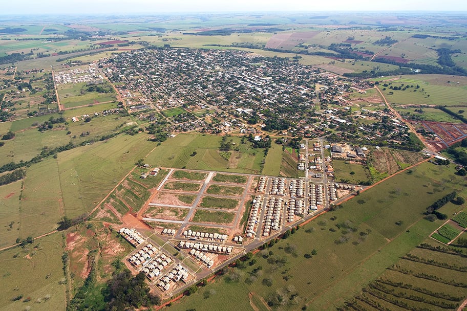 Vista aérea de um pequeno município do Sul do Brasil, com área urbana cercada por lavouras; composição horizontal e céu azul