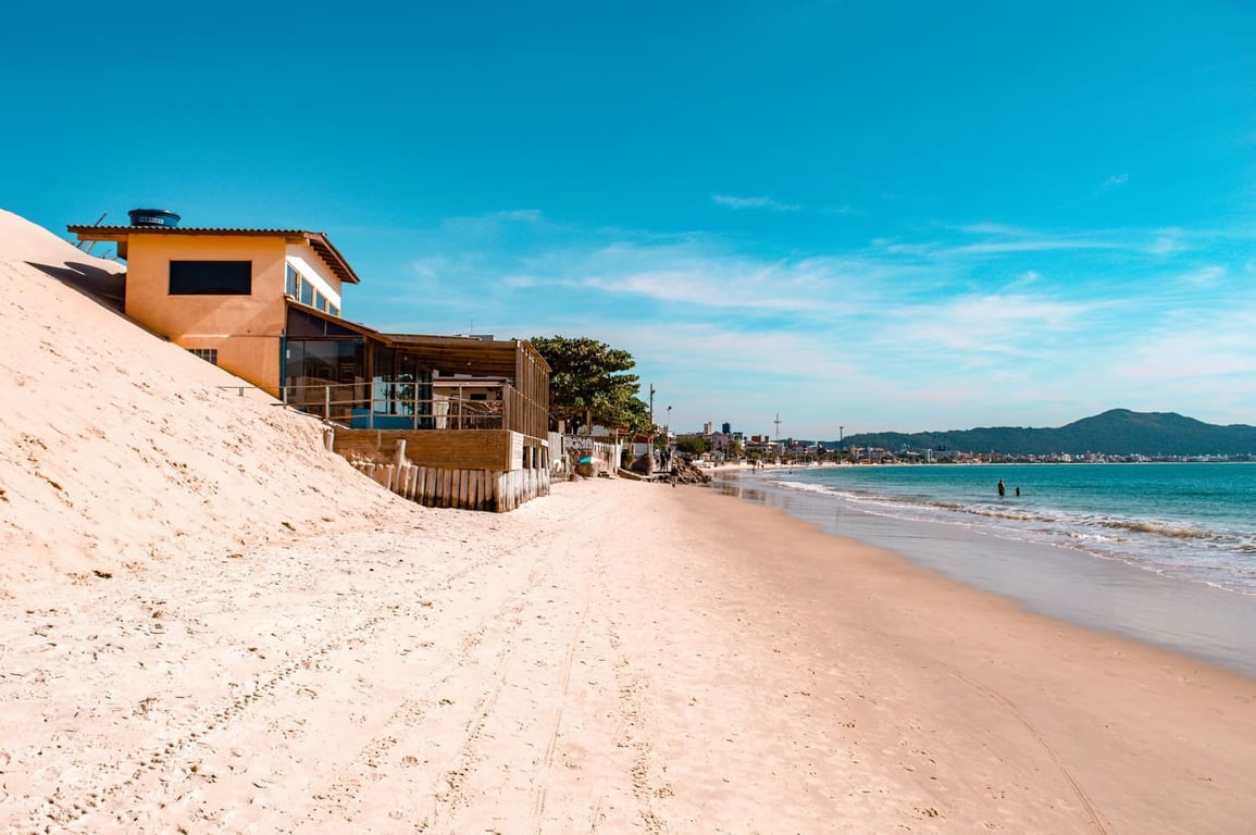 Praia no litoral sul de Santa Catarina, com faixa de areia extensa, mar azul e dunas ao fundo