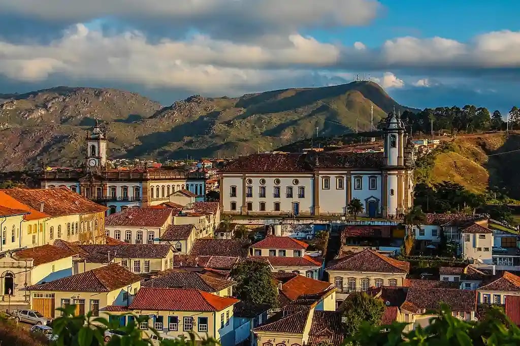 Vista aérea de Ouro Preto ao entardecer, com igrejas coloniais e montanhas ao fundo