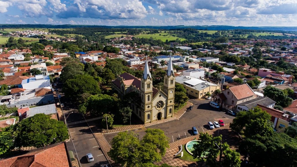 Paisagem urbana de cidade pequena do interior paulista, com igreja e casas sob céu ensolarado
