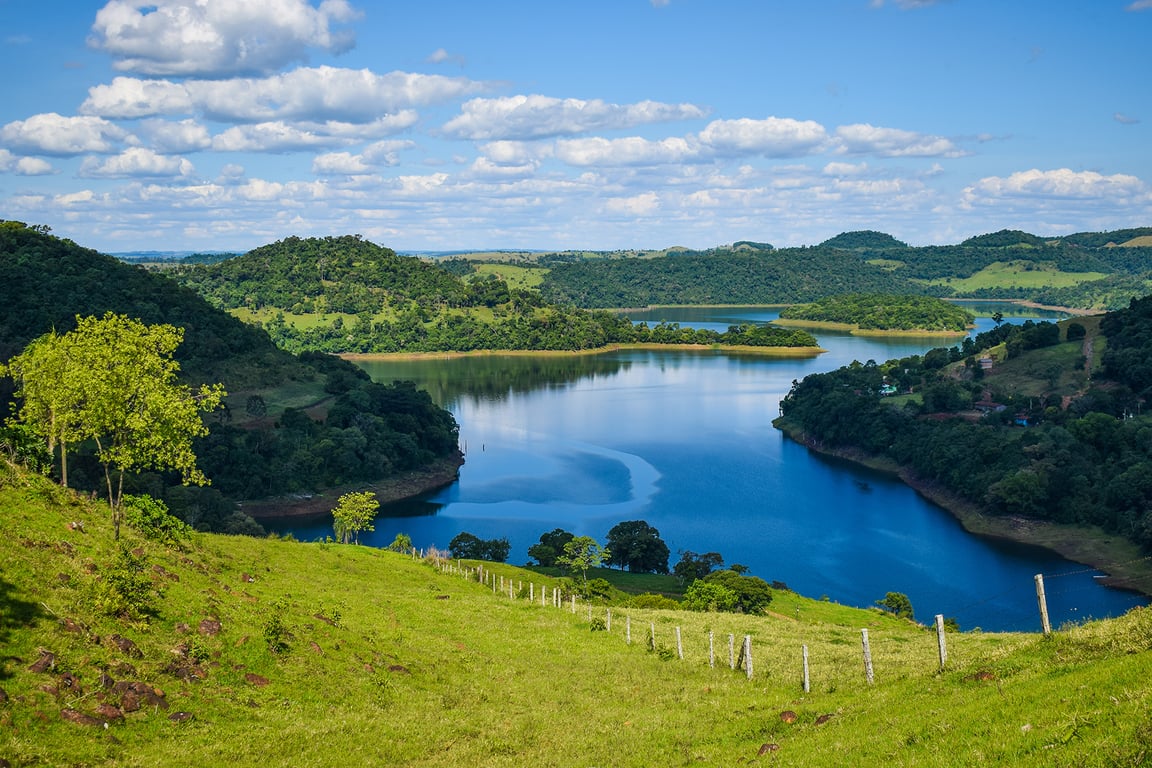 Paisagem rural do Sudoeste do Paraná com lavouras, lago e estrada vicinal sob céu amplo