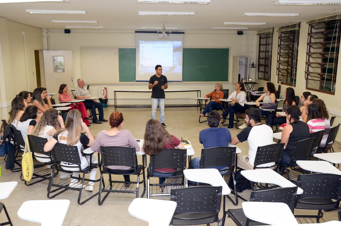 Sala de aula universitária, com professor e estudantes em atividade didática