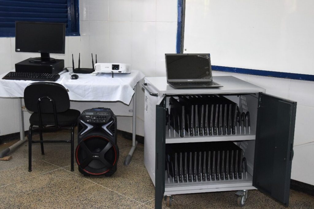 Laboratório de informática universitário, com computadores sobre bancadas e lousa ao fundo