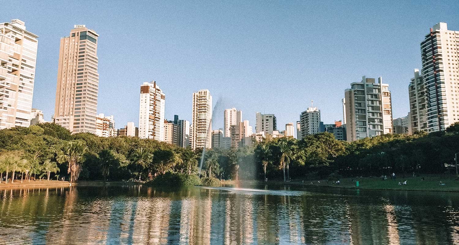 Skyline de Goiânia ao entardecer com áreas verdes e espelho d’água