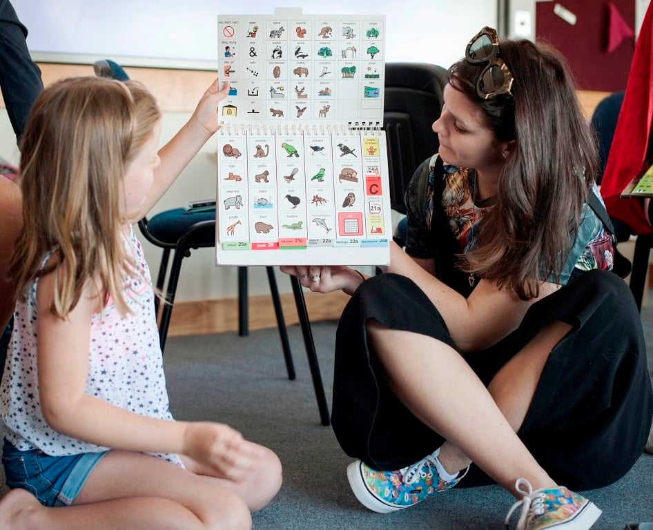 Cena ilustrativa de sala de aula inclusiva, com professora usando material visual com estudante