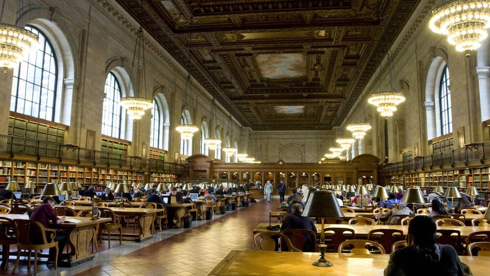 Ambiente de biblioteca universitária moderna, com estantes e estudantes em mesas de estudo iluminadas