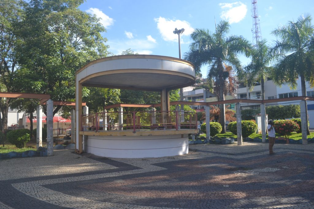 Cenário urbano arborizado, com gazebo em área pública ao fundo, em orientação horizontal