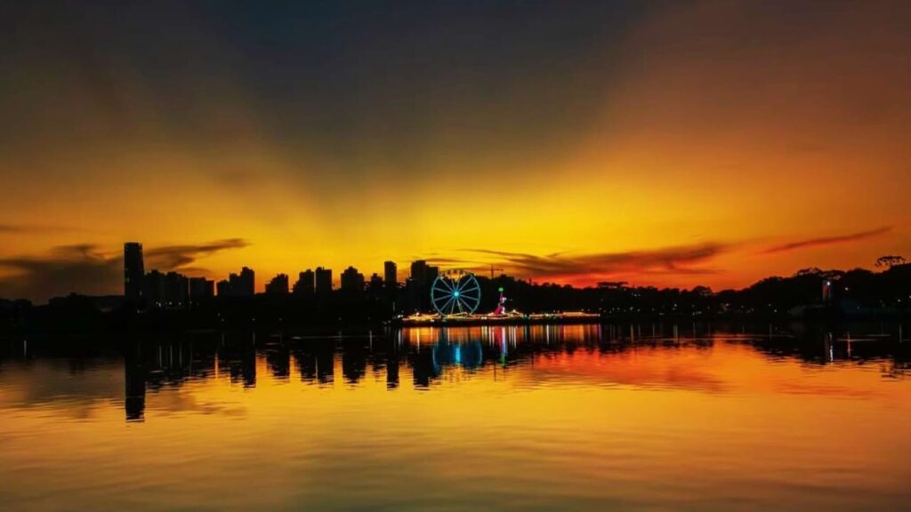 Parque Barigui em Curitiba ao pôr do sol, com lago e skyline refletidos na água