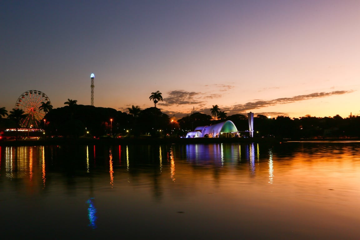 Horizonte de Belo Horizonte ao entardecer, com reflexos na água e iluminação urbana
