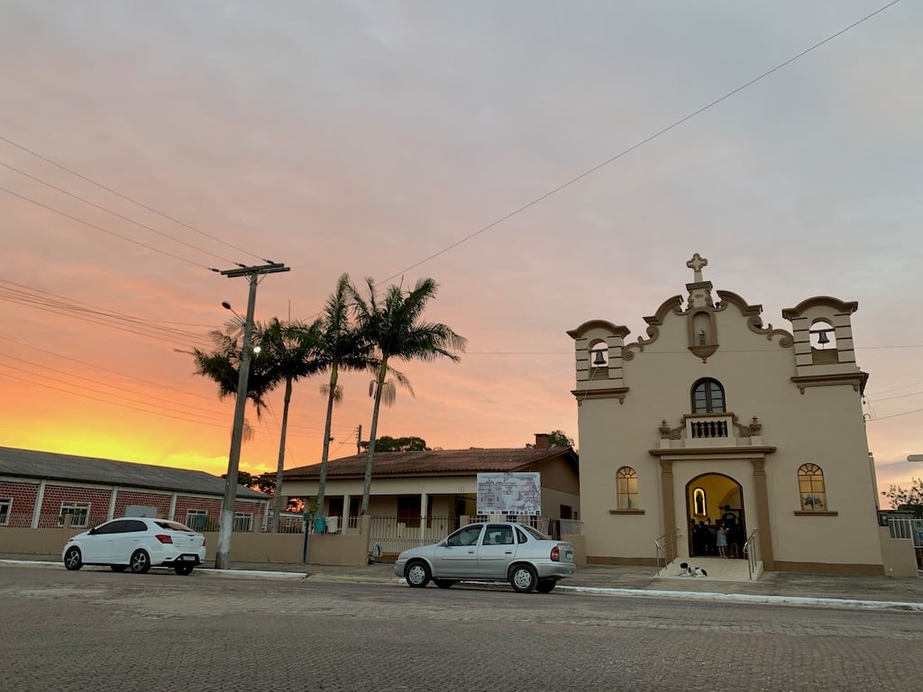 Cenário urbano de cidade pequena no litoral sul gaúcho, com igreja e comércio de rua ao entardecer