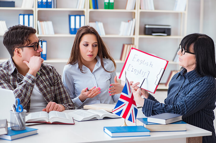 Professora conduzindo aula de inglês em sala moderna, com alunos interagindo
