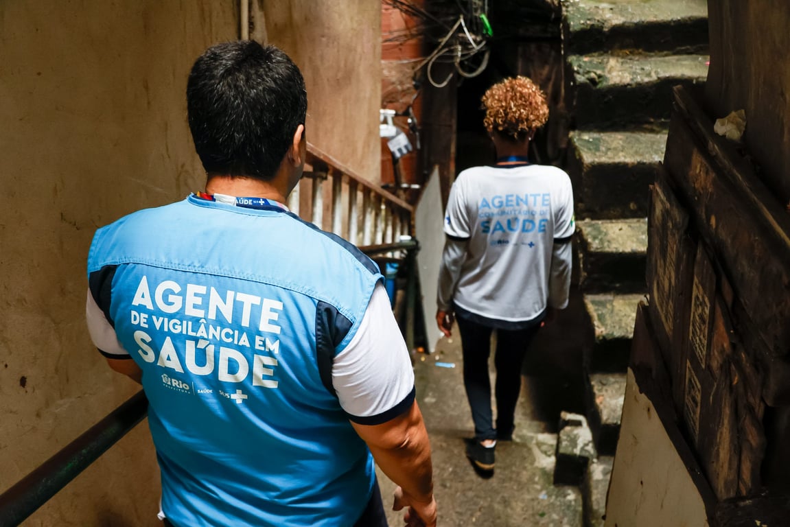 Profissionais de saúde pública em atividade de campo contra endemias, em escadaria de área urbana brasileira