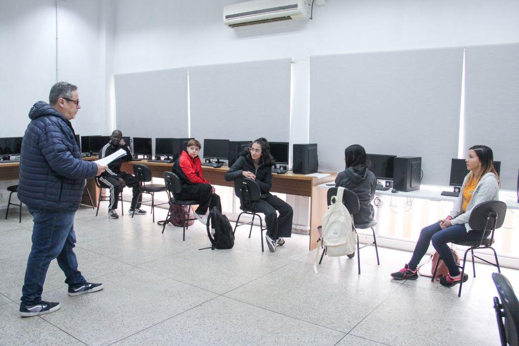 Sala de aula em curso técnico, com professor e estudantes em atividades no computador