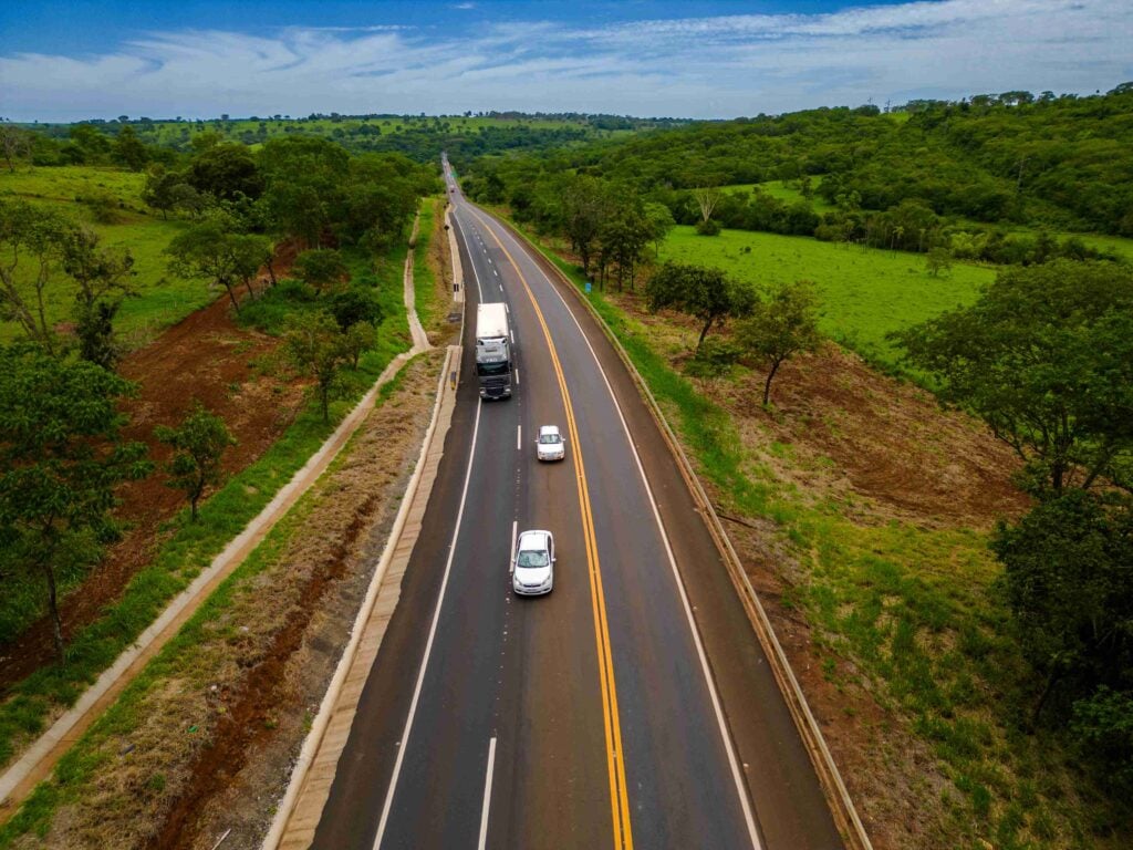 Rodovia mineira ao entardecer, com veículos em movimento, simbolizando deslocamentos regionais