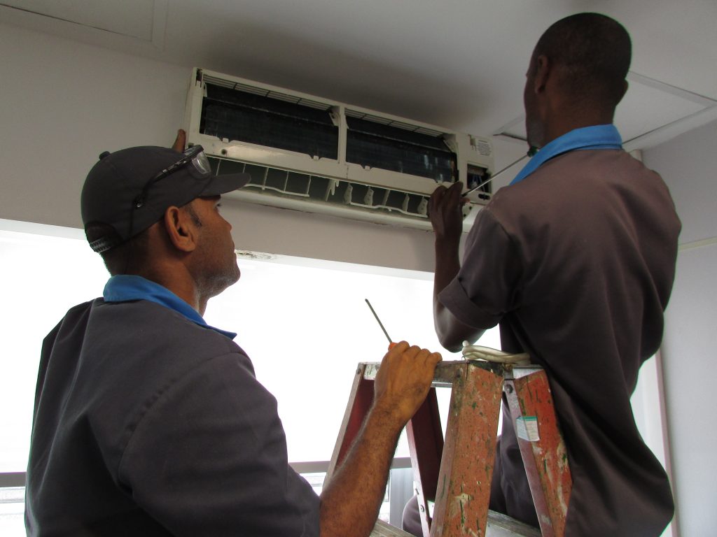 Técnicos de manutenção trabalhando em equipamento de ar-condicionado, em ambiente interno hospitalar