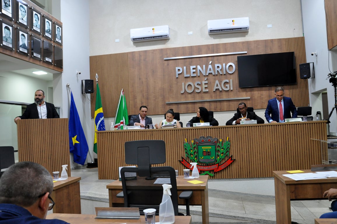 Plenário de câmara municipal com disposição de assentos e bandeiras, representando ambiente legislativo.