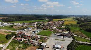 Vista aérea de Araquari com áreas urbanas e vegetação, em um dia claro. A imagem mostra a planície litorânea e o entorno de Joinville.