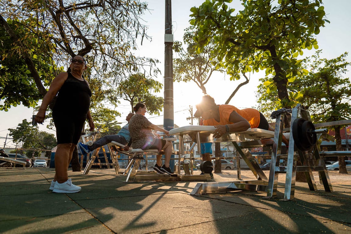 Pessoas se exercitando em academia ao ar livre, com árvores e céu aberto