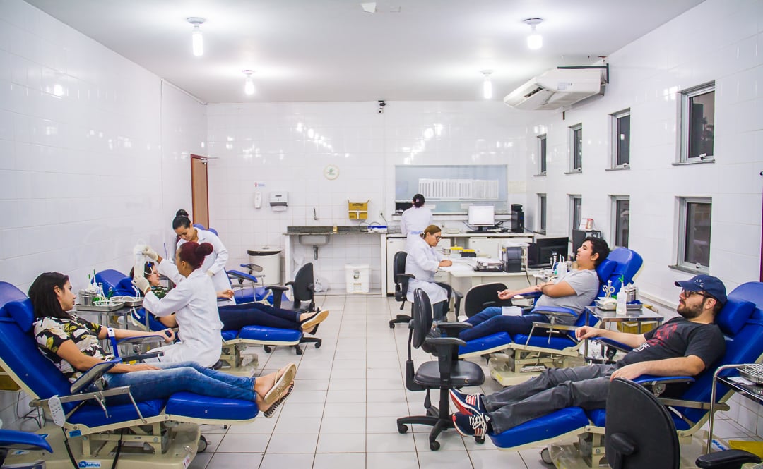 Ambiente interno de hemocentro com doadores e atendimento administrativo