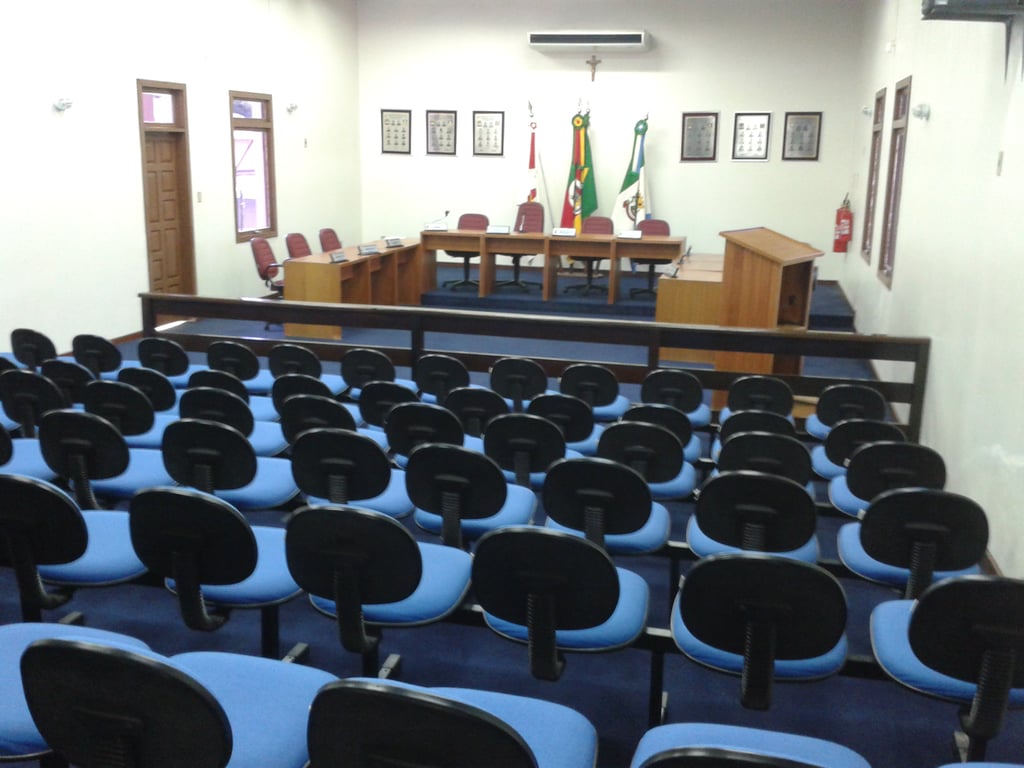 Interior de uma câmara municipal com cadeiras e mesas em plenário.