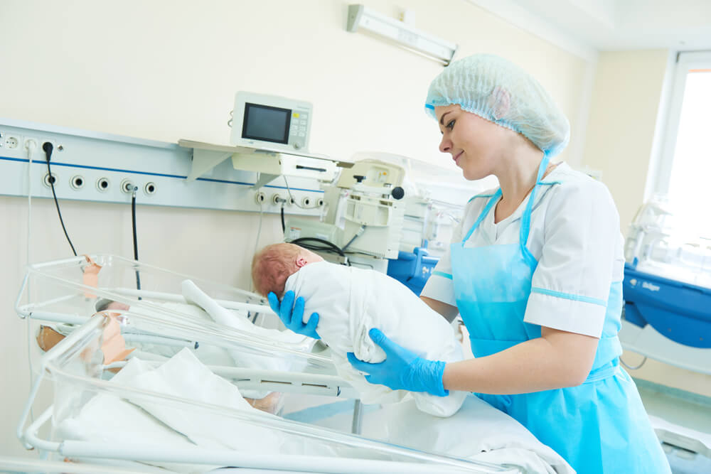 Profissional de enfermagem em ambiente de maternidade/neonatal, foco no cuidado humano, sem identificação de pacientes.
