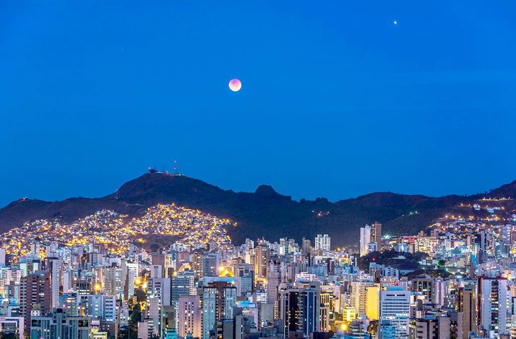 Paisagem urbana de Belo Horizonte à noite, com prédios iluminados e a Serra do Curral ao fundo