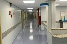 Corredor de hospital público iluminado, com equipe de enfermagem desfocada em movimento