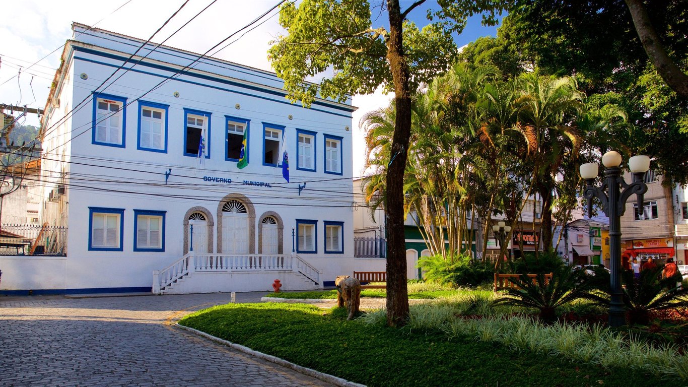 Fachada de prédio de prefeitura em cidade do Sul do Brasil com bandeiras hasteadas e jardim, em foto horizontal diurna