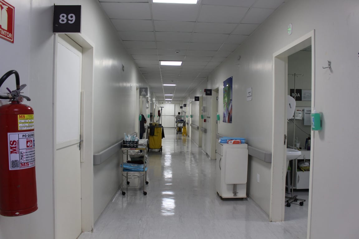 Corredor de hospital moderno, com equipe médica ao fundo e iluminação natural