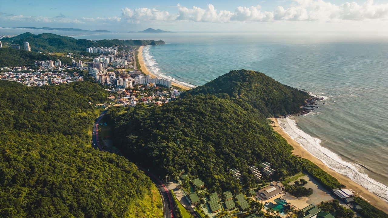 Vista aérea de Camboriú, com prédios e morros ao fundo em dia ensolarado