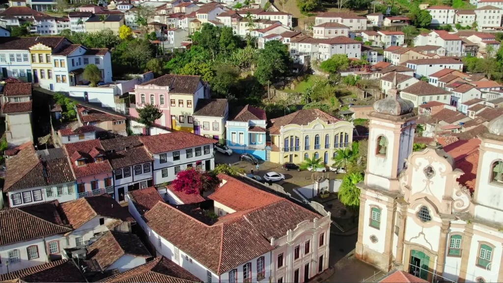 Vista aérea de cidade de médio porte com morros ao fundo ao entardecer