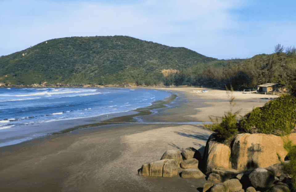 Vista do litoral de Garopaba ao entardecer, com praia, mar e morros ao fundo