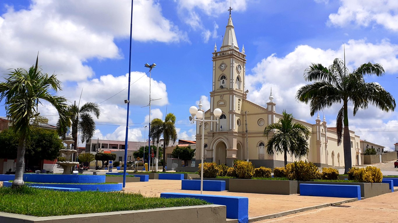 Centro urbano de uma pequena cidade do interior da Paraíba, com igreja matriz e praça central, sob céu azul