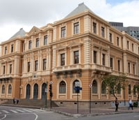 Fachada de prédio público municipal em Minas Gerais, com bandeiras hasteadas na entrada, em dia ensolarado.