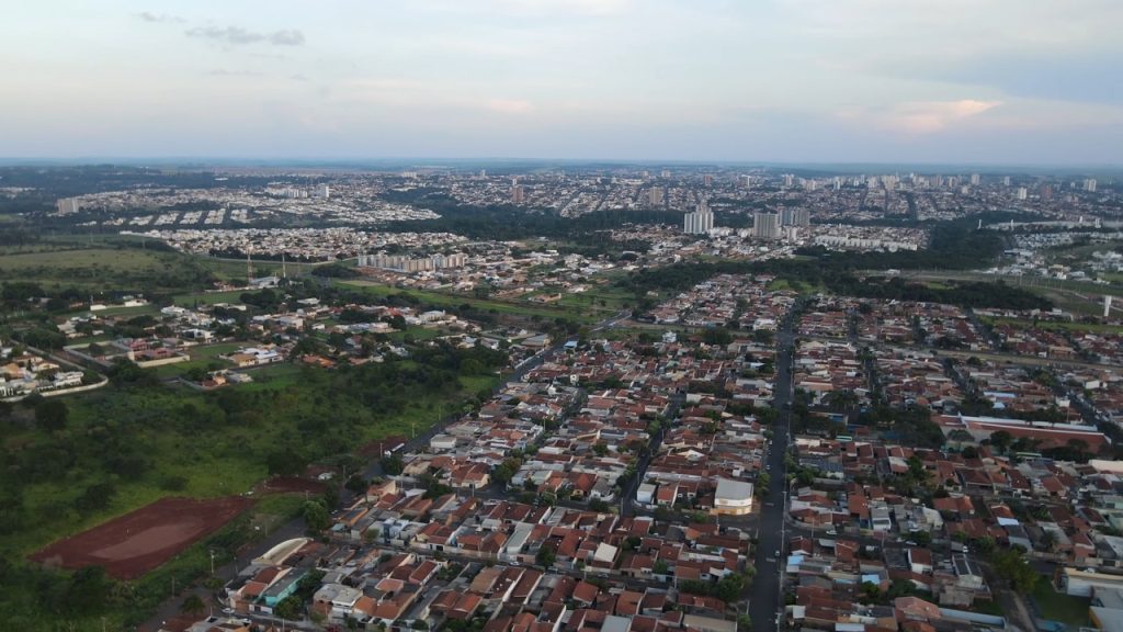 Vista aérea de cidade do interior paulista ao pôr do sol, com prédios baixos e áreas verdes
