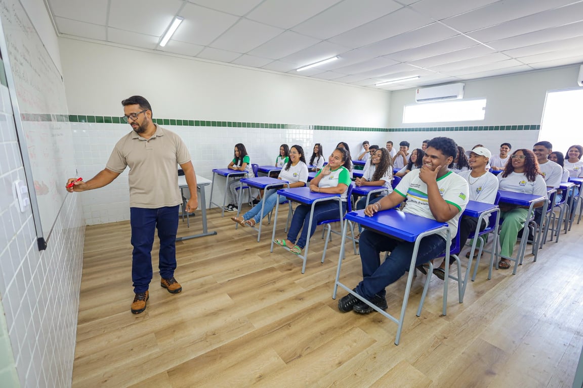 Ambiente de sala de aula em escola pública, professor ao quadro e estudantes atentos