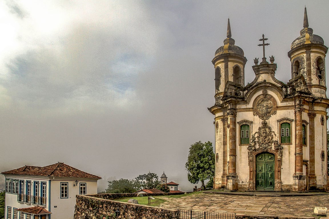 Vista panorâmica de Ouro Preto, MG, com igrejas e casario colonial ao fundo, ao entardecer