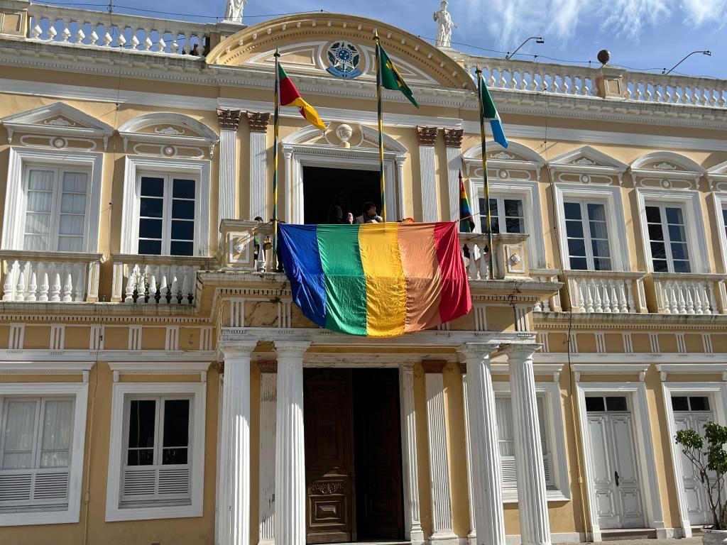 Fachada de prédio público municipal, com bandeiras hasteadas, em composição horizontal
