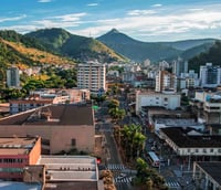 Foto aérea de Timóteo MG, com áreas urbanas e montanhas ao fundo.